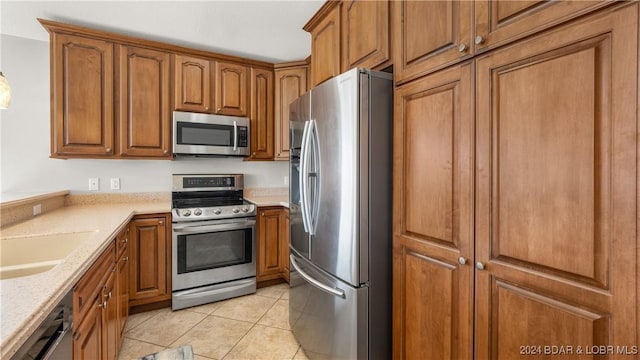 kitchen with light stone countertops, sink, light tile patterned flooring, and appliances with stainless steel finishes