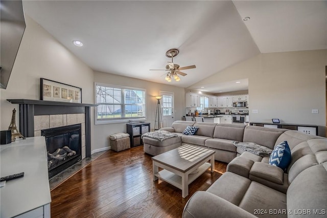 living room featuring dark hardwood / wood-style floors, ceiling fan, a tiled fireplace, and vaulted ceiling