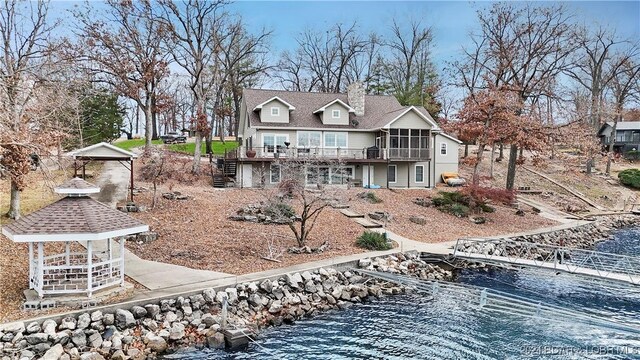 rear view of property featuring a gazebo, a sunroom, and a water view