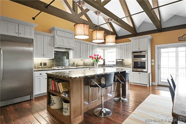 kitchen featuring a kitchen island, vaulted ceiling with beams, dark stone countertops, white cabinets, and appliances with stainless steel finishes