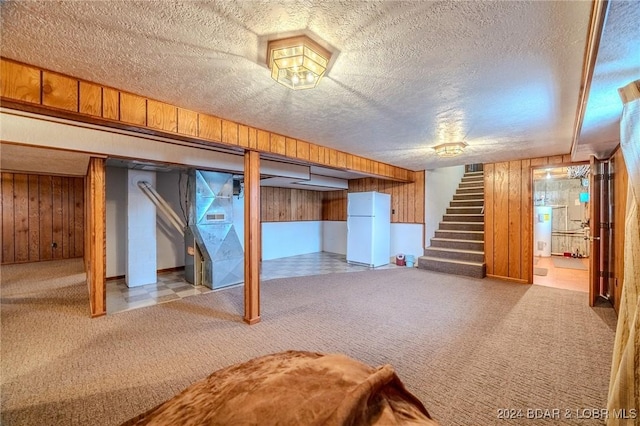 basement with carpet, wood walls, white fridge, and a textured ceiling