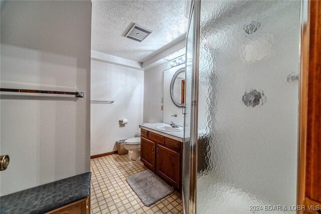 bathroom with a textured ceiling, vanity, toilet, and walk in shower