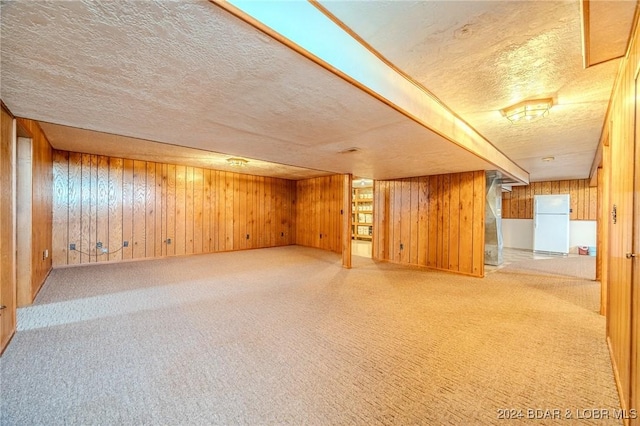 basement with carpet flooring, a textured ceiling, white fridge, and wooden walls