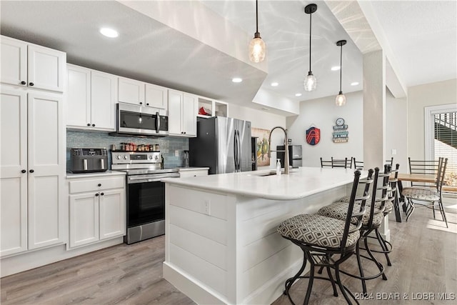 kitchen featuring appliances with stainless steel finishes, an island with sink, sink, white cabinets, and hanging light fixtures