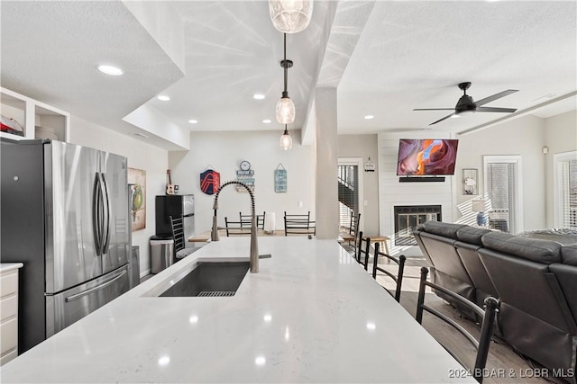 kitchen with sink, stainless steel fridge, ceiling fan, hanging light fixtures, and a fireplace