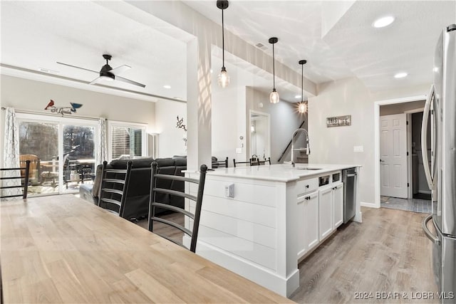 kitchen with sink, white cabinetry, decorative light fixtures, appliances with stainless steel finishes, and light hardwood / wood-style floors