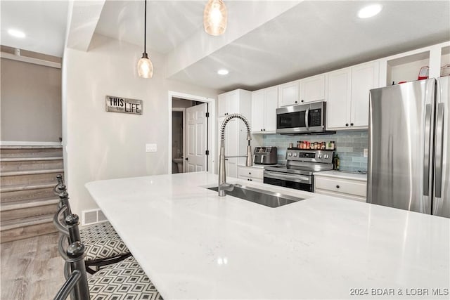 kitchen with sink, backsplash, pendant lighting, stainless steel appliances, and white cabinets