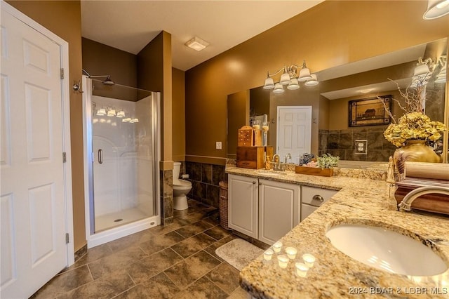 bathroom with vanity, a shower with shower door, tile walls, and toilet