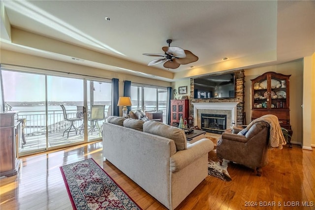 living room with hardwood / wood-style floors, a water view, ceiling fan, and a tray ceiling