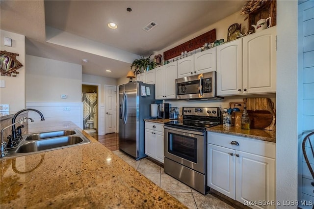 kitchen with appliances with stainless steel finishes, dark stone counters, sink, white cabinets, and light tile patterned flooring