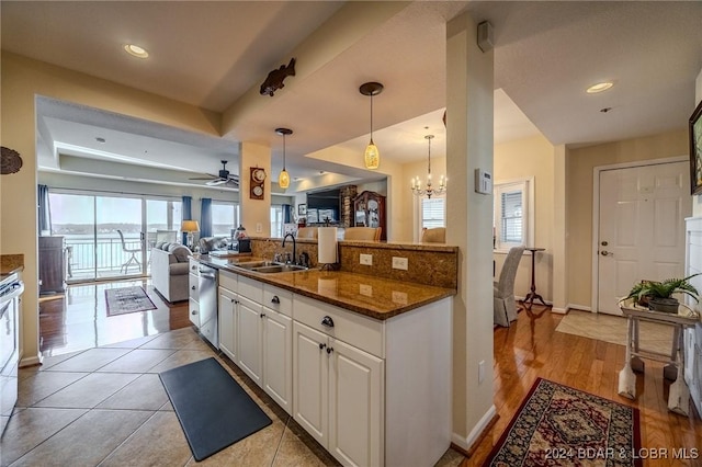 kitchen featuring dishwasher, dark stone counters, white cabinets, sink, and decorative light fixtures