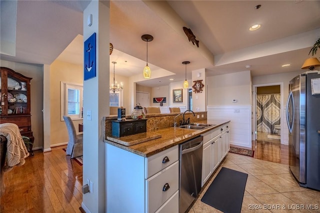 kitchen with appliances with stainless steel finishes, sink, pendant lighting, an inviting chandelier, and white cabinetry