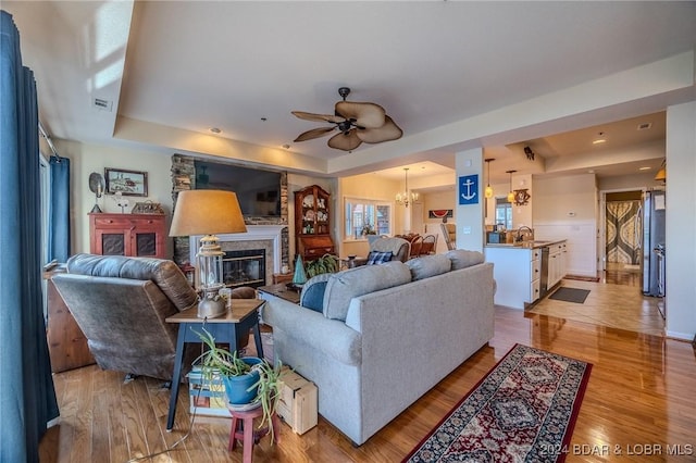 living room with ceiling fan with notable chandelier, light wood-type flooring, sink, and a tray ceiling