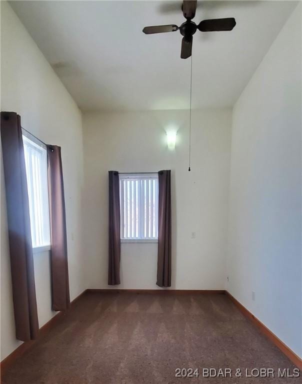 empty room featuring dark colored carpet, ceiling fan, and a wealth of natural light