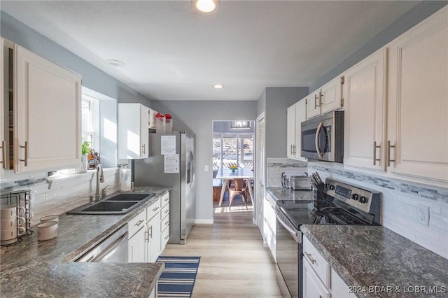 kitchen featuring white cabinetry, sink, backsplash, light hardwood / wood-style floors, and appliances with stainless steel finishes