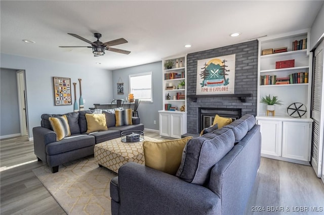 living room featuring ceiling fan, wood-type flooring, and a brick fireplace