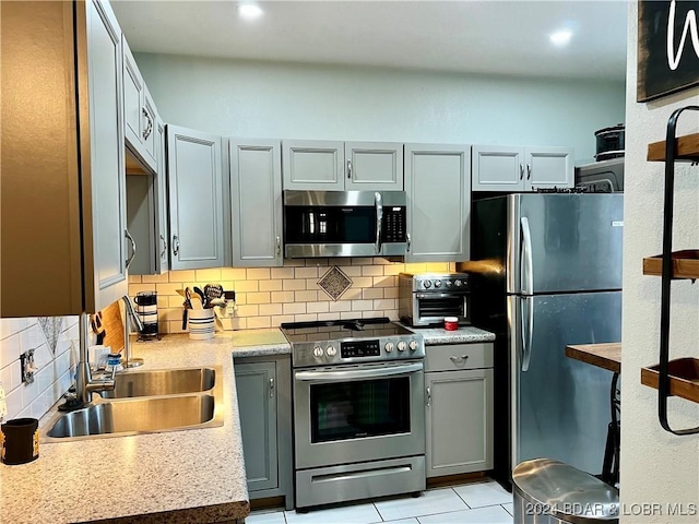 kitchen with tasteful backsplash, gray cabinets, sink, and appliances with stainless steel finishes