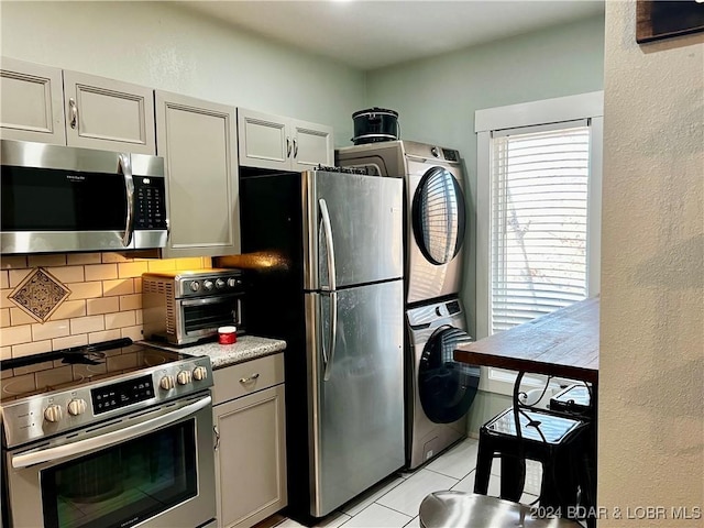 kitchen with tasteful backsplash, gray cabinetry, stainless steel appliances, stacked washer / dryer, and light tile patterned flooring