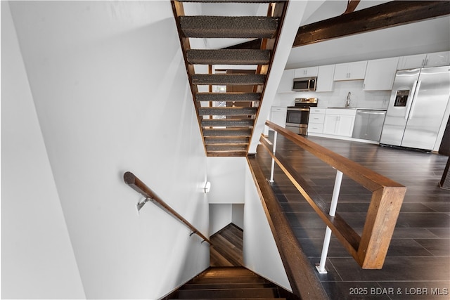 stairway featuring beam ceiling, sink, and wood-type flooring