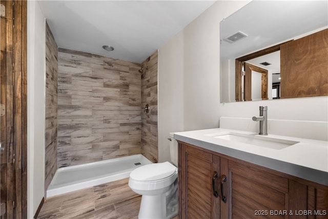 bathroom with tiled shower, vanity, and toilet