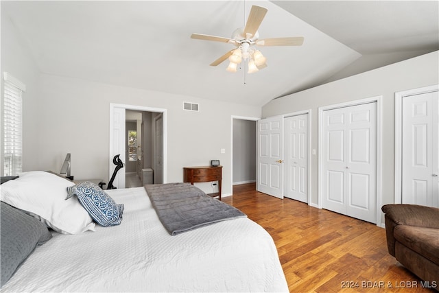 bedroom with two closets, hardwood / wood-style flooring, vaulted ceiling, and ceiling fan