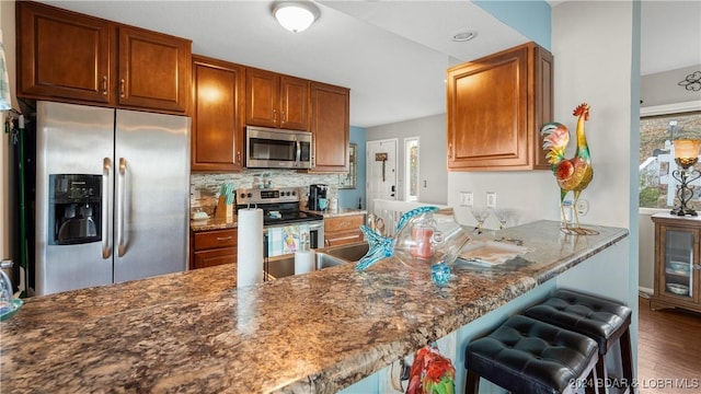 kitchen featuring backsplash, stone counters, appliances with stainless steel finishes, a kitchen bar, and kitchen peninsula