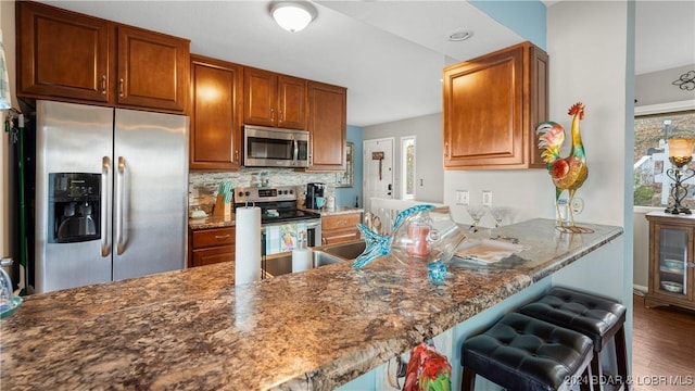 469 Staniel Cay Dr, Osage Beach, MO 65065 - kitchen with appliances with stainless steel finishes, wood finished floors, a breakfast bar, backsplash, and brown cabinets