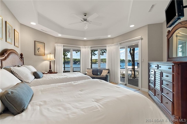 bedroom with ceiling fan, a water view, access to outside, and a tray ceiling