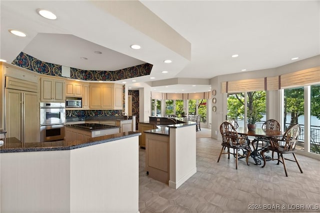 kitchen with a center island, dark stone counters, a raised ceiling, built in appliances, and kitchen peninsula