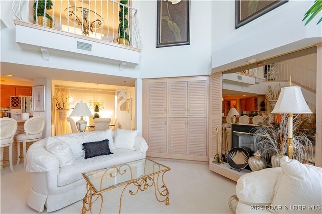 living area with a fireplace with raised hearth, visible vents, and a towering ceiling