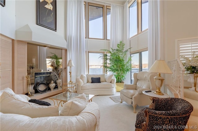 carpeted living room with a towering ceiling and a glass covered fireplace