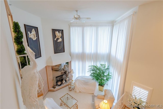 sitting room with a ceiling fan, a fireplace with raised hearth, and a wealth of natural light