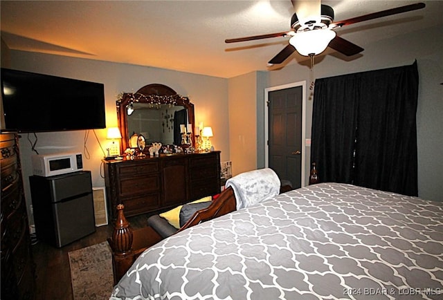 bedroom with dark hardwood / wood-style floors, black fridge, and ceiling fan