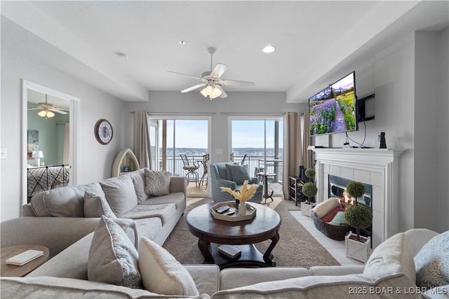 living room with a tiled fireplace, ceiling fan, and light tile patterned flooring