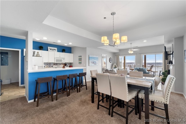 dining area featuring light carpet, ceiling fan with notable chandelier, and a raised ceiling