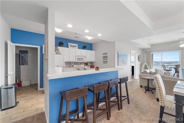 kitchen with white appliances, kitchen peninsula, decorative backsplash, white cabinetry, and a breakfast bar area