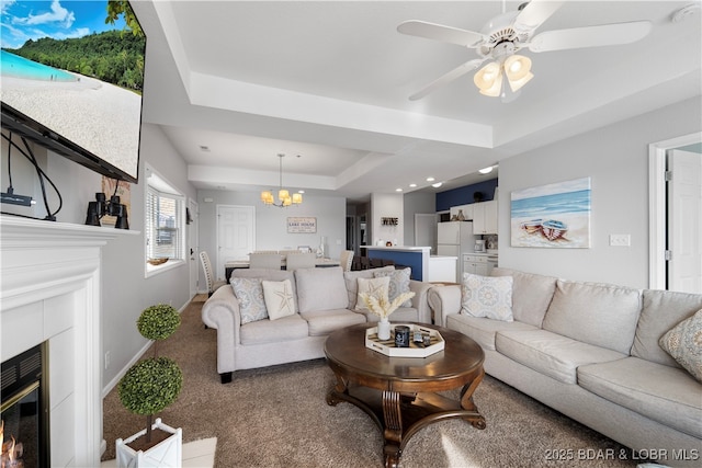 carpeted living room with ceiling fan with notable chandelier and a tray ceiling