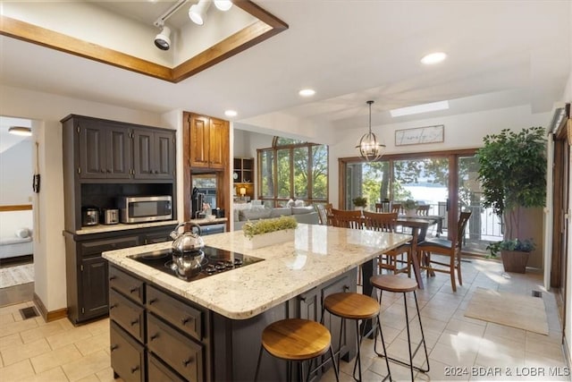 kitchen featuring light stone countertops, black electric stovetop, a chandelier, a breakfast bar, and a kitchen island