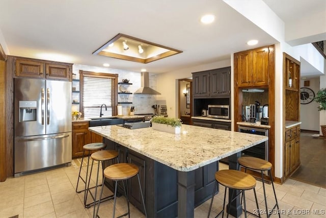 kitchen with appliances with stainless steel finishes, a center island, a kitchen breakfast bar, and wall chimney range hood