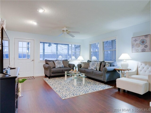 living room with a textured ceiling, ceiling fan, and dark wood-type flooring