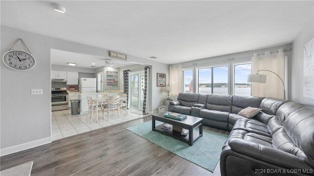 living room featuring light wood-style floors, baseboards, ceiling fan, and a water view