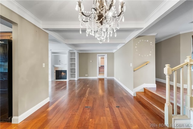 unfurnished living room with ornamental molding, beam ceiling, built in features, a notable chandelier, and hardwood / wood-style floors