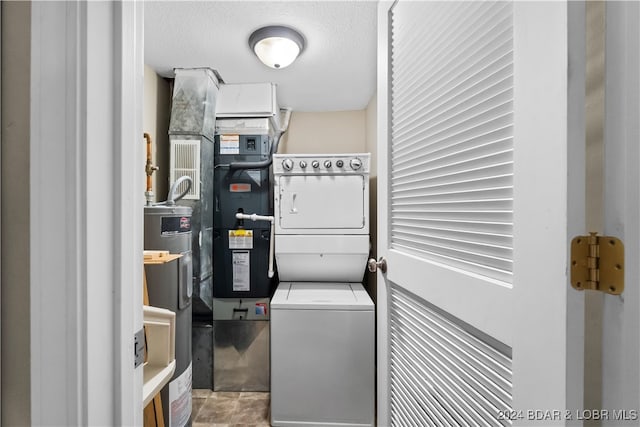 washroom with a textured ceiling, electric water heater, and stacked washer / drying machine