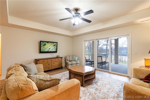 living room with light hardwood / wood-style flooring, a raised ceiling, and ceiling fan