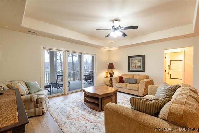 living room with a tray ceiling, ceiling fan, and light wood-type flooring