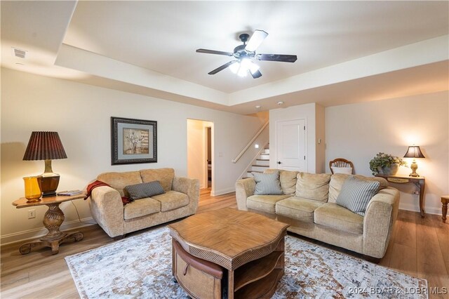 living room with light wood-type flooring, a tray ceiling, and ceiling fan