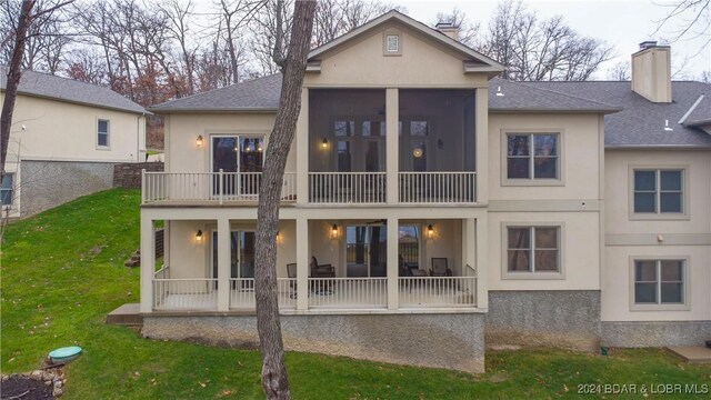 rear view of property with a sunroom, a balcony, and a lawn