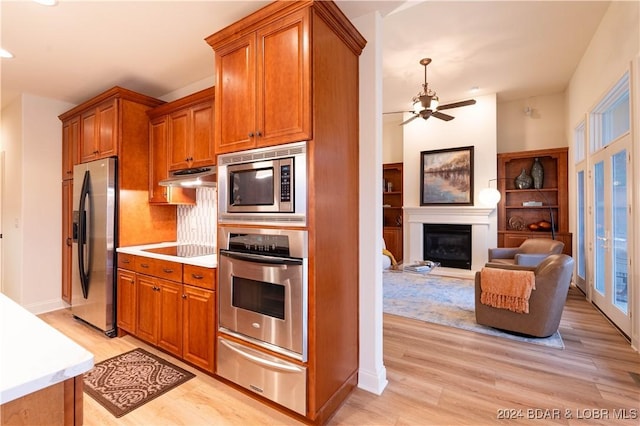 kitchen with under cabinet range hood, appliances with stainless steel finishes, brown cabinets, a warming drawer, and a glass covered fireplace