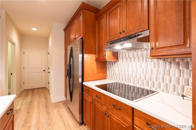 kitchen featuring brown cabinets, under cabinet range hood, stainless steel fridge, and black electric cooktop