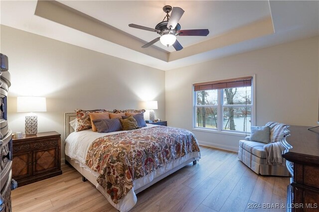 bedroom featuring light hardwood / wood-style floors, a raised ceiling, and ceiling fan